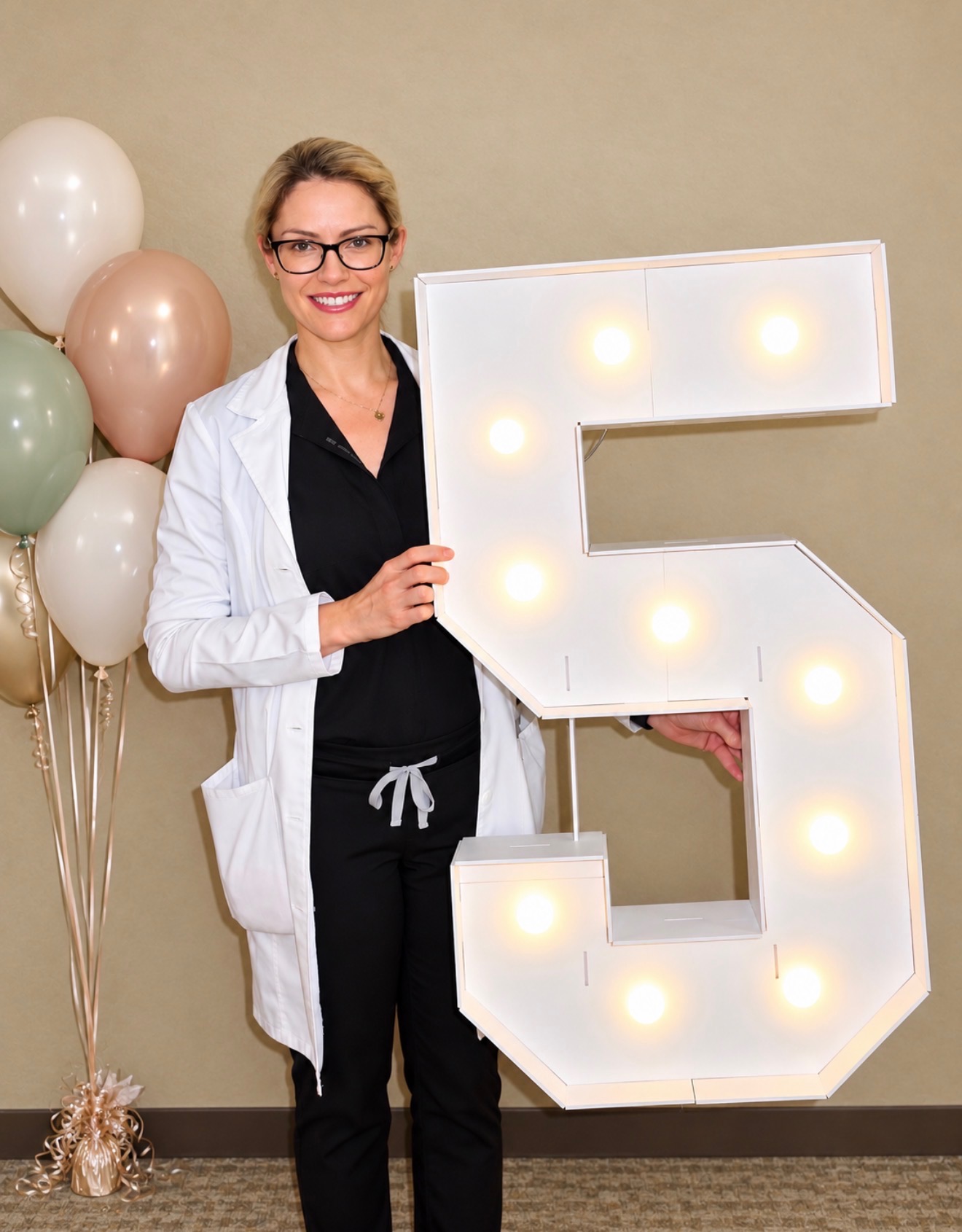 Dr. Harvey 5-Year Anniversary Dr. Harvey smiling and holding a lighted number 5 sign beside balloons, celebrating five years at Fox Valley Ophthalmology